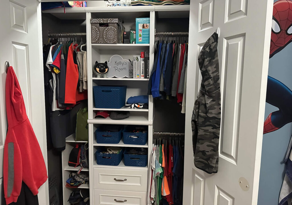 A neatly organized closet with hanging clothes, shelves of books and storage bins, and a sign labeled "Kelly's Room."