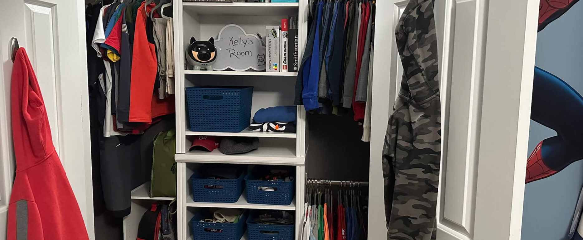 A neatly organized closet with hanging clothes, shelves of books and storage bins, and a sign labeled "Kelly's Room."