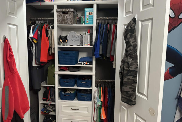 A neatly organized closet with hanging clothes, shelves of books and storage bins, and a sign labeled "Kelly's Room."