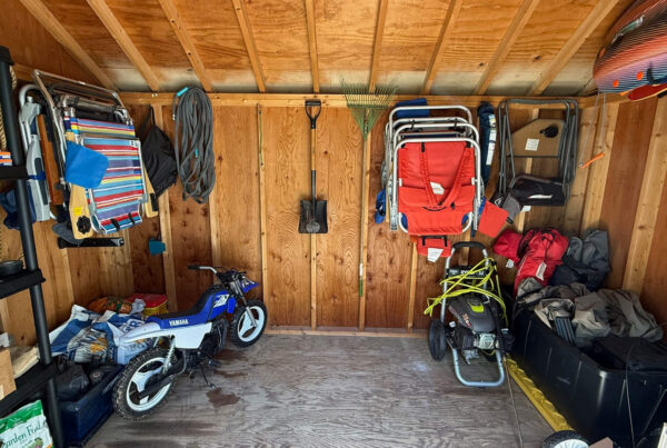 A wooden garage interior with tools, a toy bike, folding chairs, a snowblower, and various outdoor gear hanging and stored