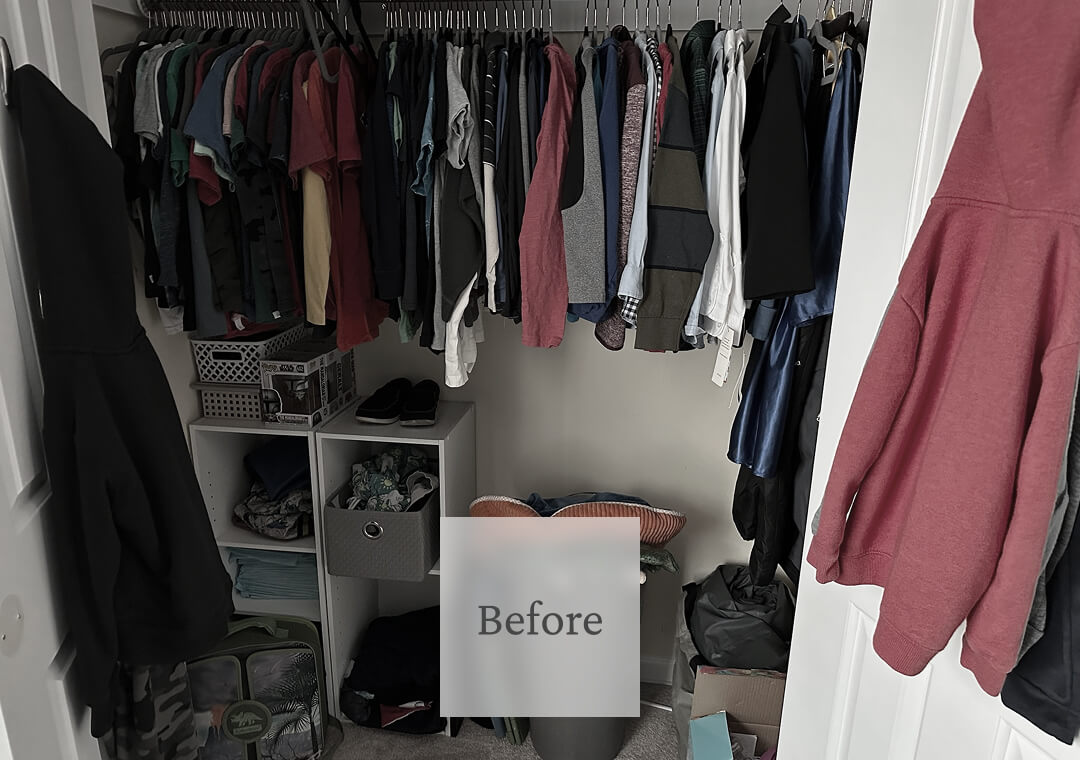 Clothes hang on a rod in a cluttered closet, with shoes, storage bins, and a pillow on the floor.